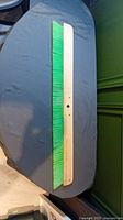 Photo of the full length of the 3 foot concrete broom showing wooden base and green bristles lying on a table.
