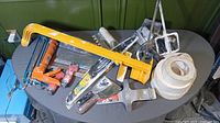 Drywall tools including multiple knives, rolls of drywall tape and mesh, caulking tool, manual tape dispenser, and other accessories on table