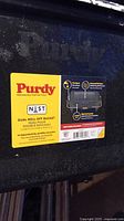 Photo showing Purdy brand label on the outside of the black plastic dual roll-off paint bucket with product details.