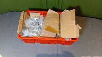 Orange crate with multiple boxes containing plastic bags of metal door installation parts including hinges and screws