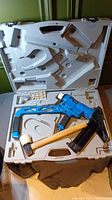 Gray molded plastic case opened showing blue flooring nailer and wooden mallet.