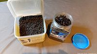 Two containers of black phosphate coated pan head framing screws, one large bucket and one smaller jar with blue lid removed showing screws inside.
