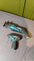 Makita cordless reciprocating saw and compact impact driver laid on grey surface