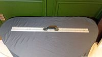 Full view of 36-inch metal straight edge ruler with black handle placed horizontally on a gray surface.