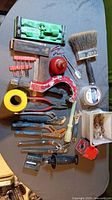 Overview photo showing all items including paintbrush, clamps, pliers, tape, screws and measuring tape laid out on surface