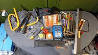Full view of tool assortment on a table including hacksaws, coping saw, tape measures, bolt cutters, rivet tool, drill bits, and hand tools.