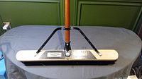 Full front view of the broom head showing wooden base and metal support braces with attached handle.