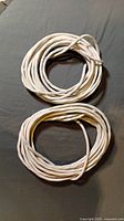 Photo of two coiled lengths of white Romex wire on a dark surface.
