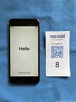 Front view of iPhone 6 displaying Hello screen indicating initial setup mode, next to Maxsold auction number 8 ticket.