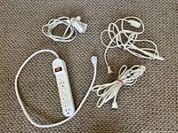 Three white cords including a white power strip with four outlets and an on/off switch, displayed on carpeted floor.