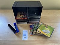 Black storage box with several CDs and some loose CD cases spread out on table.