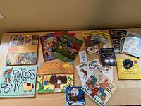 Collection of children's books including Princess Tales, Curious George, Robert Munsch, Goldilocks with puppets displayed on a wooden table.