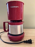 Front view of the Cuisinart red coffeemaker unit with stainless steel carafe attached and power cord laid out on wood surface.