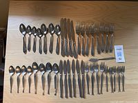 Overview of both steel cutlery sets laid out side-by-side showing knives, forks, spoons, and teaspoons for each set.