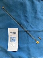 Full shot of the 18-inch gold tone chain necklace with two pendants - Infant Jesus of Prague pendant attached and a separate 10K gold cross pendant laid on blue fabric.