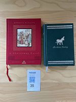 Two hardcover books side by side on a wooden background, the titles are 'A Christmas Carol' in red and 'The Silver Donkey' in green.