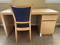 Desk and chair front view showing light pine desk with side cabinet on right and chair with blue fabric upholstery.