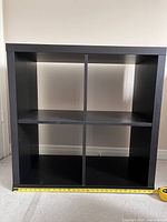 Black-brown IKEA shelf unit with four compartments, visible measuring tape showing width.
