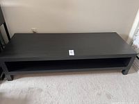 Front view of black-brown IKEA TV bench with one open shelf and four legs.