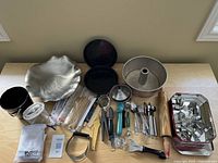 Overview of the assortment of kitchen and bakeware items including pans, cookie cutters, utensils, rolling pin, and skewers laid out on a table.