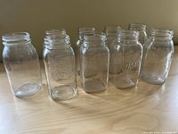 Front view of nine medium-sized glass jars, showing six Mason jars with visible embossed branding.