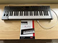Nektar Impact LX49+ MIDI controller keyboard and user guide laid on wooden surface with connected USB cable.