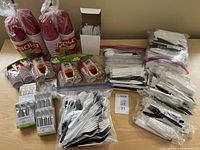 Overview of large and small red SOLO plastic cups, sets of white plastic cutlery (forks, spoons, knives) in clear bags and retail packaging, plus a box of white drinking straws.