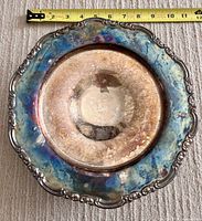Top view of tarnished silver-plated serving salver/platter showing ornate floral border and scalloped edge against carpet background with tape measure indicating size.