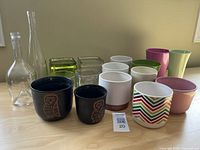 Full lot of 14 small decorative plant pots and vases arranged on a wooden surface, including ceramic, glass, and metal items in various colors and shapes.