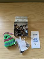 Photo of box containing various polished stones and beads, a green and pink drawstring pouch, a white organza pouch with smaller stones, and a MaxSold lot number card.