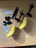 Photo showing the full lot items arranged on table: pair of yellow shoe stretchers, black bunion plugs, shoehorn and instruction sheet.