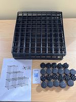 Stack of black wire grid panels alongside round corner connectors and printed instruction sheet showing sample cube shelf configuration.