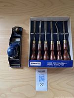 Full view of 6 wooden handled wood carving tools in original box and a blue metal hand plane