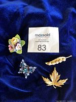 All four brooches laid out on a dark blue fabric background with MaxSold lot number for identification