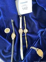 Four vintage watches displayed on a dark blue fabric, showing different band styles and sizes.