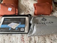 Photo showing two sets of burnt orange decorative pillows, a packaged Living brand cooling memory foam pillow, and a Parkview pillow cover bag on floral beige duvet cover