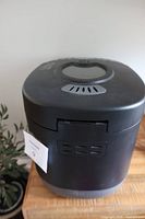 Top and side view of black Hamilton Beach HomeBaker bread maker showing vent and viewing window on lid.