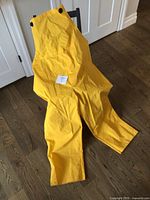 Yellow rain pants laid out on wood floor showing adjustable straps and construction