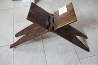 Photo showing front angle of wooden Turkish prayer bench with folded legs and carved details on sides.