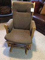 Front view of a wooden framed gliding rocker chair with brown upholstered seat and backrest, padded armrests.