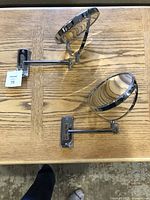 Two chrome wall-mounted magnifying mirrors laid flat on a wooden surface showing side views and adjustable arms.