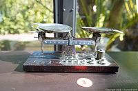 Front side view of the antique balance scale showing metal pans, balance beam scale markings, and weights on wooden base.
