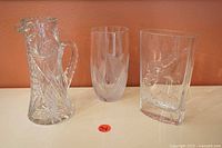 Three crystal items: pitcher on left, cylindrical vase middle, rectangular vase right