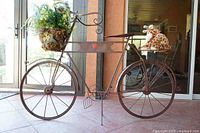 Side profile showing entire decorative bicycle plant stand with artificial plant in front basket and giraffe plush on back seat.