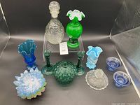 Overview of entire glassware lot arranged with Fenton green overlay tulip vase, etched Wexford decanter, blue and white slag vase, small cobalt bowls, and covered dishes