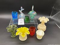 Nine assorted vintage glass art pieces displayed on black background with clear riser for height variation