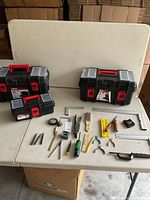 Overview of three black plastic toolboxes with red latches and handles, along with assortment of hand tools laid out on the table.