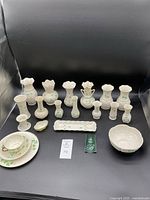 Full set of vintage Belleek pieces arranged on black background showing variety of small vases, cup and saucer, bowl and trays all with green shamrock decoration.