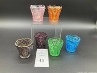 Front view of six multicolored carnival glass toothpick holders arranged on black background with display riser.