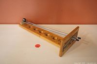 Front angle showing the wooden game base with seven ball slots and metal rods with steel ball.